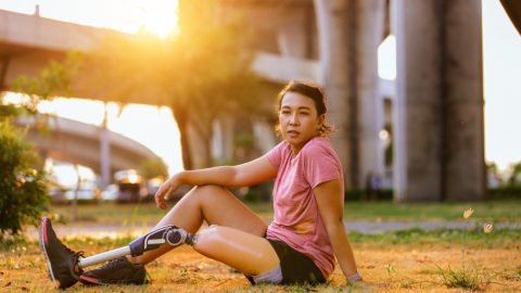 Athlete with prosthetic leg doing warm up exercise on park